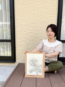 光藤有佳（Yuka Mitsufuji）がバラの花のデッサン画を持って座っている写真、アート作品、手描きデッサン Photo of Yuka Mitsufuji holding a rose flower sketch while sitting, art piece, hand-drawn illustration 光藤有佳（Yuka Mitsufuji）坐著拿著玫瑰花素描畫的藝術家照片，藝術作品，手繪素描